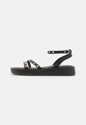 Sort platformsandal med ankelrem og tåremme, hver dekoreret med sølvfarvede runde nitter og en sølvspænde på ankelremmen.