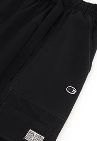 Zwarte shorts met een elastische tailleband, voorzien van een witte geborduurde logo en een labelpatch. Zachte textuur met zichtbare stikseldetails.