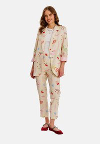 Kremowy garnitur z fantazyjnymi wzorami w odcieniach różu, zieleni i niebieskiego. Marynarka ma luźny krój i podwinięte mankiety; spodnie są zwężane.