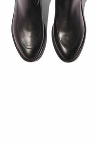 Un par de zapatos de vestir de cuero negro pulido con punteras puntiagudas sobre un fondo blanco, vistos desde arriba.
