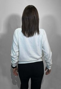 Maglione bianco con superficie testurizzata, maniche stile felpa e orlo a costine, abbinato a pantaloni neri. Visto da dietro.
