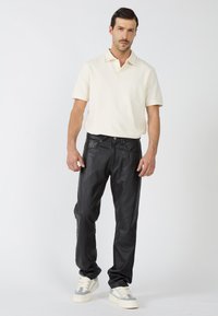 Schwarze Lederhosen mit lockerer Passform, kombiniert mit einem hellen Creme-Polohemd. Die Sneaker haben graue Akzente und eine cremefarbene Sohle.