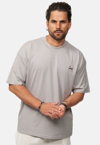 Helles graues Kurzarm-T-Shirt aus Baumwolle mit Rundhalsausschnitt. Hat ein kleines, buntes Logo auf der Brust. Glatte Textur.