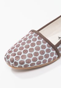 Chaussure plate en tissu avec des pois marron, une bordure marron et une semelle beige, présentée en gros plan au niveau des orteils.