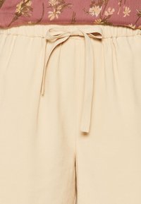 Pantaloni beige con vita elastica e cintura annodata. Tessuto liscio, leggero, taglio dritto, dotati di tasche laterali. Adatti per abbigliamento casual.