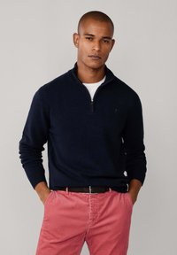 Marineblaue Zip-up-Sweatjacke mit langen Ärmeln, gerippten Bündchen und einem leichten Kragen, kombiniert mit rosa Cordhosen und einem schwarzen Gürtel.