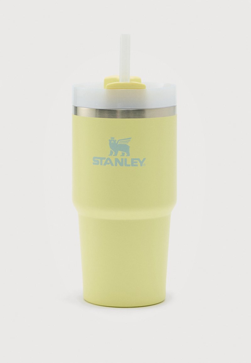 Κίτρινο μονωμένο ποτήρι Stanley με διαφανές καπάκι και λευκό καλαμάκι, ανοξείδωτη στεφάνη και λογότυπο με λέοντα με φτερά στο μπροστινό μέρος.