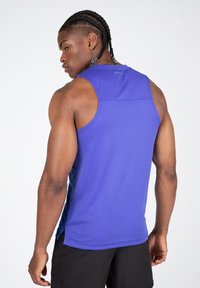 Kelių rankovių sportinė tank top žavi mėlyna spalva, pagaminta iš lengvos medžiagos, su plokščiomis siūlėmis ir šiek tiek pailginta nugaros dalimi, užtikrinančia komfortą.