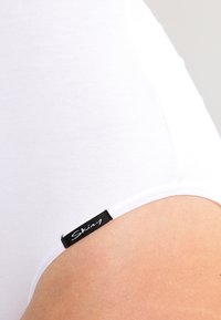 Slip bianco in cotone con una texture liscia e un'etichetta nera con il nome del marchio "Skiny" cucita all'elastico della vita.