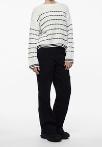 Biały sweter z dzianiny z czarnymi paskami, ściągaczami przy mankietach i dolnym brzegu. W zestawie czarne spodnie cargo z bocznymi kieszeniami i luźnym krojem.