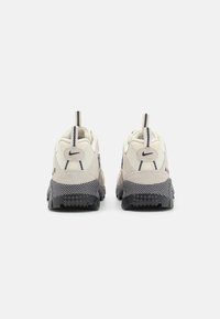 Nike Air sneakers in off-white and black with textured mesh and suede details. Features a padded collar and distinctive outsole pattern.