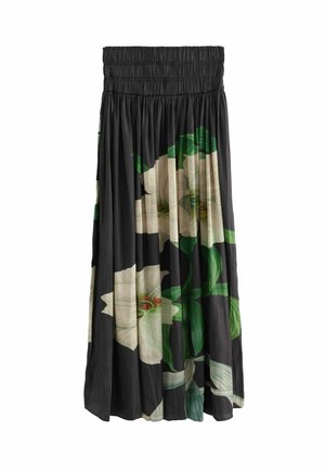 Femme marchant dans une robe noire fluide avec de grandes impressions de fleurs blanches, portant des bottines et un bracelet en argent dans un cadre urbain.