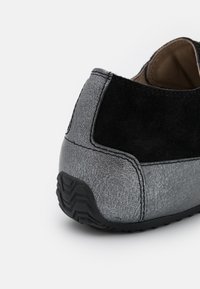 Grå och svart läder sneakers häldetalj med texturerad sula och synlig sömnad på vit bakgrund.