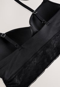 Bralette negru cu bretele reglabile, cupe moi și margine din dantelă de-a lungul marginii inferioare.