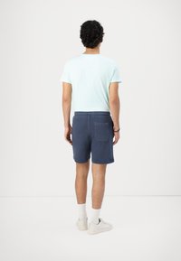 Lyseblå kortærmet t-shirt kombineret med marineblå shorts med en baglomme. Hvide sneakers og ankelsokker fuldender outfittet.