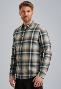 Camisa de cuadros de manga larga en beige, azul marino y gris, con un diseño de botón, textura de tela suave y detalle del logo central en el pecho.