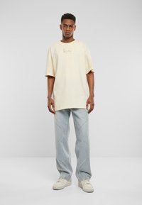 Light yellow oversized t-shirt with a subtle logo, paired with light blue wide-leg jeans featuring curved stitch detailing and neutral sneakers.