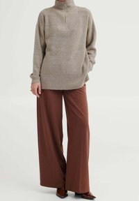 Pull en maille côtelée beige avec un col montant et une fermeture éclair, associé à un pantalon large marron et des chaussures à bout pointu marron.
