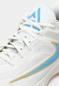 Witte sportieve schoen met een gestructureerde bovenkant, lichtblauwe accenten en een blauw logo op de tong. Heeft platte veters en een rubberen zool.