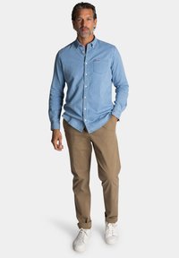 Lichtblauw denim overhemd met knopen en een borstzak, gecombineerd met beige broeken en witte sneakers. Casual ontwerp en een relaxte pasvorm.
