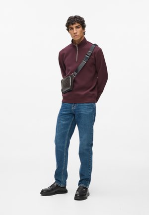 Burgundská mikina na zip, modré džíny, černé kožené boty a černá kabelka přes rameno s texturovaným vzorem. Jednoduchý, moderní design.