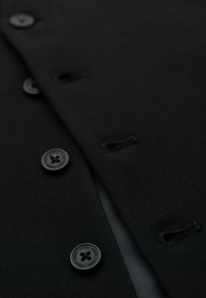 Close-up van zwarte jasstof met knoopsgaten en zwarte knopen met de tekst "Ombre", waarbij de textuur en sluitdetails worden benadrukt.