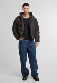 Zwarte gewatteerde jas met hoge kraag, relaxte pasvorm, gedragen over een zwarte top, gecombineerd met losse blauwe spijkerbroek en zwarte schoenen.