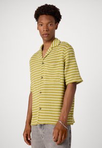 Chemise à manches courtes, col en vert clair avec des rayures blanches, avec une poche avant et une fermeture à boutons. Fabriquée en tissu texturé.