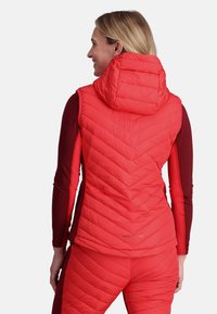 Rote isolierte Steppweste mit Kapuze, ausgestattet mit Rautensteppung und einem taillierten Design, kombiniert mit einem dunkelroten Langarmoberteil.