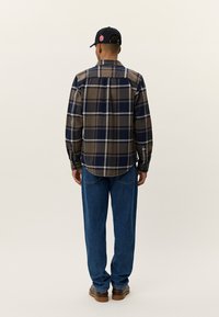 Bruine en blauwe geblokte shirt met lange mouwen, knoopsluiting kraag en afgeronde zoom, gecombineerd met blauwe jeans en bruine laarzen.