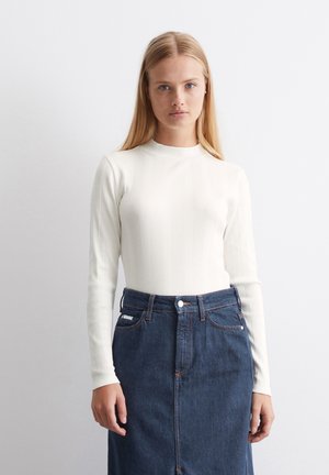 Weißes, geripptes Langarmoberteil mit hohem Kragen, kombiniert mit einem hoch taillierten Denimrock. Der Rock verfügt über eine vordere Knopfverschluss und Taschen.