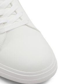 Sneaker bianco con superiore sintetico liscio, chiusura con lacci, punta arrotondata e suola in gomma; design minimalista senza motivi o accenti visibili.