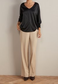 Blusa nera in satin con scollatura a V e maniche a tre quarti, abbinata a pantaloni beige a gamba larga e tacchi a punta scuri.