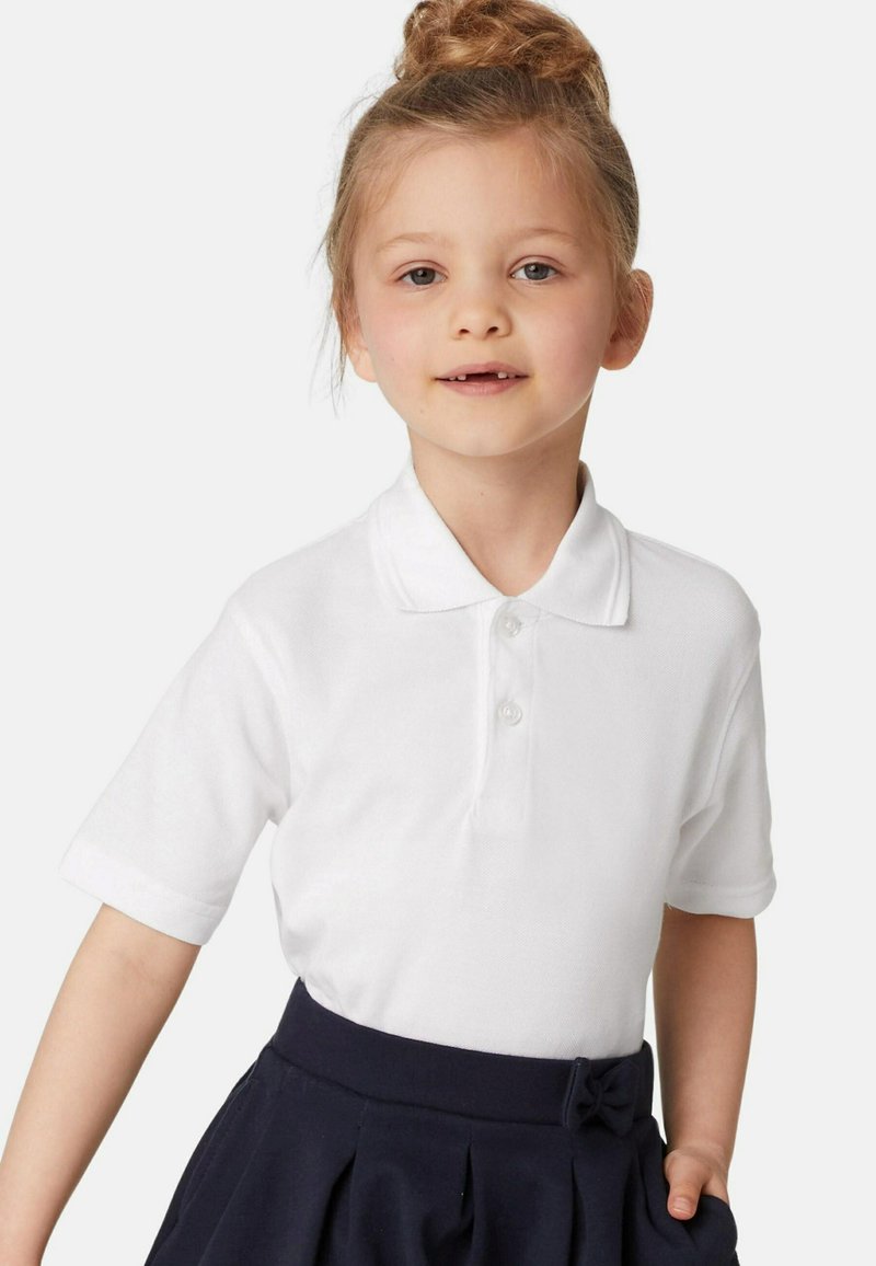 Polo bianco con due bottoni, abbinato a una gonna a pieghe blu navy con un dettaglio a fiocco in vita. Tessuto dalla superficie liscia.
