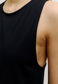 Schwarzes ärmelloses Top aus weichem Stoff, mit rundem Ausschnitt und sichtbaren Nähten entlang der Kanten, in einem klaren, minimalistischen Design.
