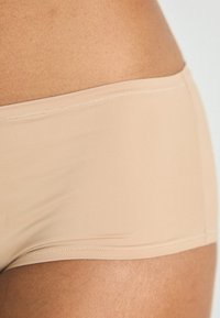 Beige sømløse hipster-truse laget av elastisk stoff med en glatt tekstur og subtil søm langs kantene.