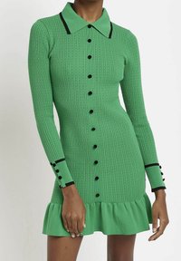 Robe verte à côtes avec un col, accents de boutons noirs, manches longues et ourlet volanté. Tissu texturé avec des lignes verticales.