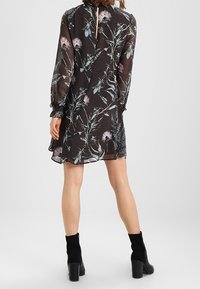 Schwarzes florales Kleid mit langen Ärmeln, einem Schlüsselloch-Rücken, leichtem Stoff und bunten Blumenmustern in Rosa- und Grüntönen.