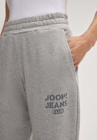 Graue Jogginghose aus weichem Stoff, mit einem elastischen Bund und Seitentaschen. Auf der Vorderseite befindet sich ein bedrucktes Logo in Dunkelgrau.