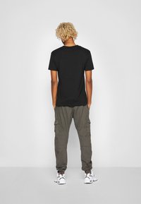 Zwart T-shirt met korte mouwen gecombineerd met olijfgroene cargobroek met zakken en witte sneakers. De algehele look is casual en functioneel.