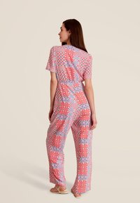 Combinaison à motifs rouges et bleus avec des manches courtes, taille élastique, jambes larges et accents floraux, fabriquée en tissu léger.