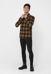 Zwarte en gele geblokte flanellen overhemd met button-down kraag, gecombineerd met zwarte skinny broek en zwarte enkelboots.