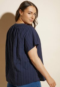 Top blu navy a maniche corte con strisce verticali testurizzate, scollatura plissettata e vestibilità morbida, abbinato a jeans in denim.