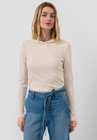 Beige gerippter Kapuzenpullover mit langen Ärmeln und dezentem Muster; kombiniert mit hoch taillierten blauen Denim-Jeans mit Bindegürtel-Detail.