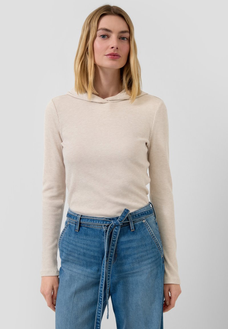 Beige gerippter Kapuzenpullover mit langen Ärmeln und dezentem Muster; kombiniert mit hoch taillierten blauen Denim-Jeans mit Bindegürtel-Detail.