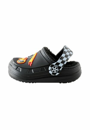 Black slip-on shoe with fuzzy interior, featuring colorful flame and wheel embellishments; textured rubber outsole and checkered strap.