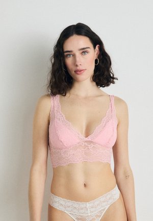 Lace bralette i lys rosa med brede stropper og flagrande kanter, kombinert med en matchende lace truse, som har en myk tekstur og delikat mønster.