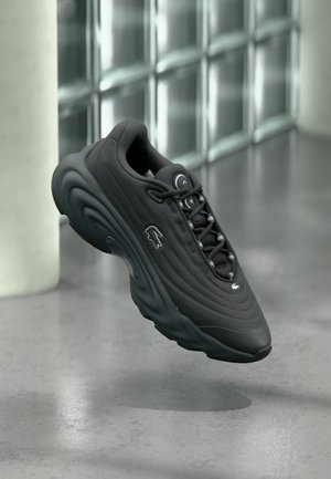 Black sneaker with a textured upper, curved sole, and reflective accents. Features a logo on the side and lace-up design.