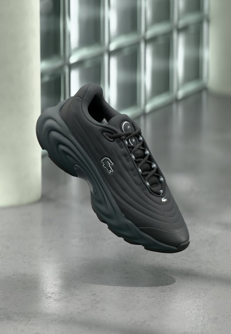 Sort sneaker med tekstureret overdel, buet sål og reflekterende detaljer. Har en logo på siden og snørelukning.