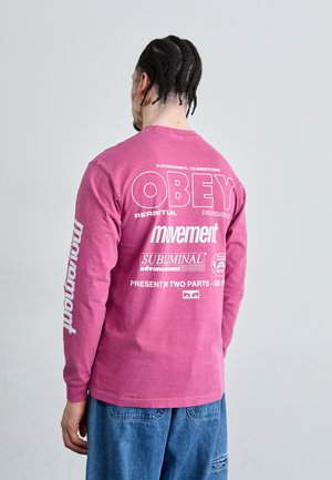 Langärmliges, pinkes Baumwoll-T-Shirt mit großen weißen Schriftzügen, Markenzeichen und Phrasen auf dem Rücken und dem Ärmel, lockere Passform, hüftlang.